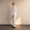 View 4 of product A person with curly hair wears the Turnbull and The Deck White Cotton Minimalist Shirt by Turnbull & Asser, paired with pants. Posed against a plain background, their minimalist silhouette is highlighted in this black and white image.