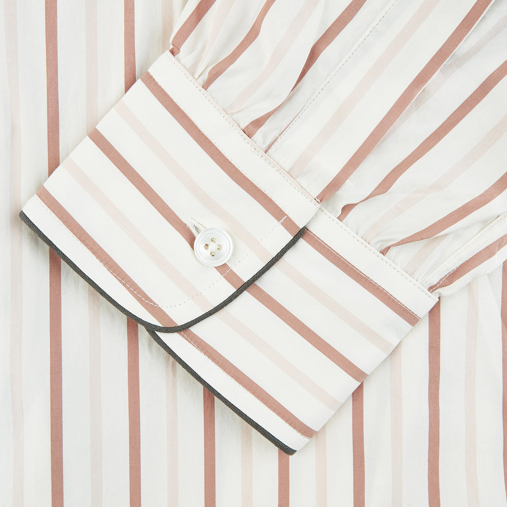The Burgundy Multi Striped Cotton Sussex Nightshirt by Turnbull & Asser features long sleeves, knee length, a pointed collar, chest pocket, burgundy and beige stripes on white, buttoned cuffs, and a curved hem for classic sleepwear style.