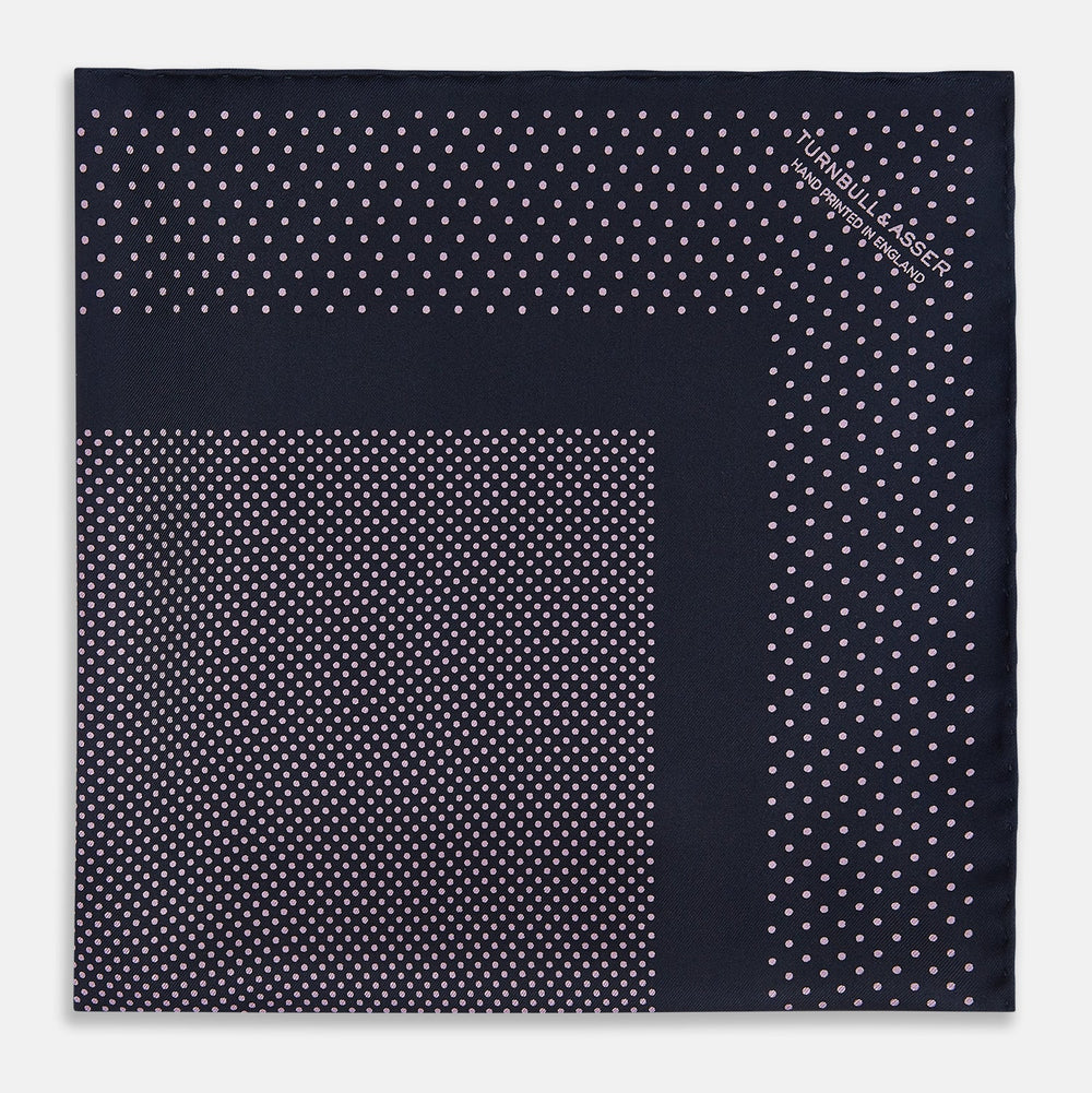 The Turnbull & Asser Navy and Lilac Dot Silk Pocket Square features small white polka dots with a wider border of spaced-out dots, neatly folded to showcase both sides of its handmade silk fabric.