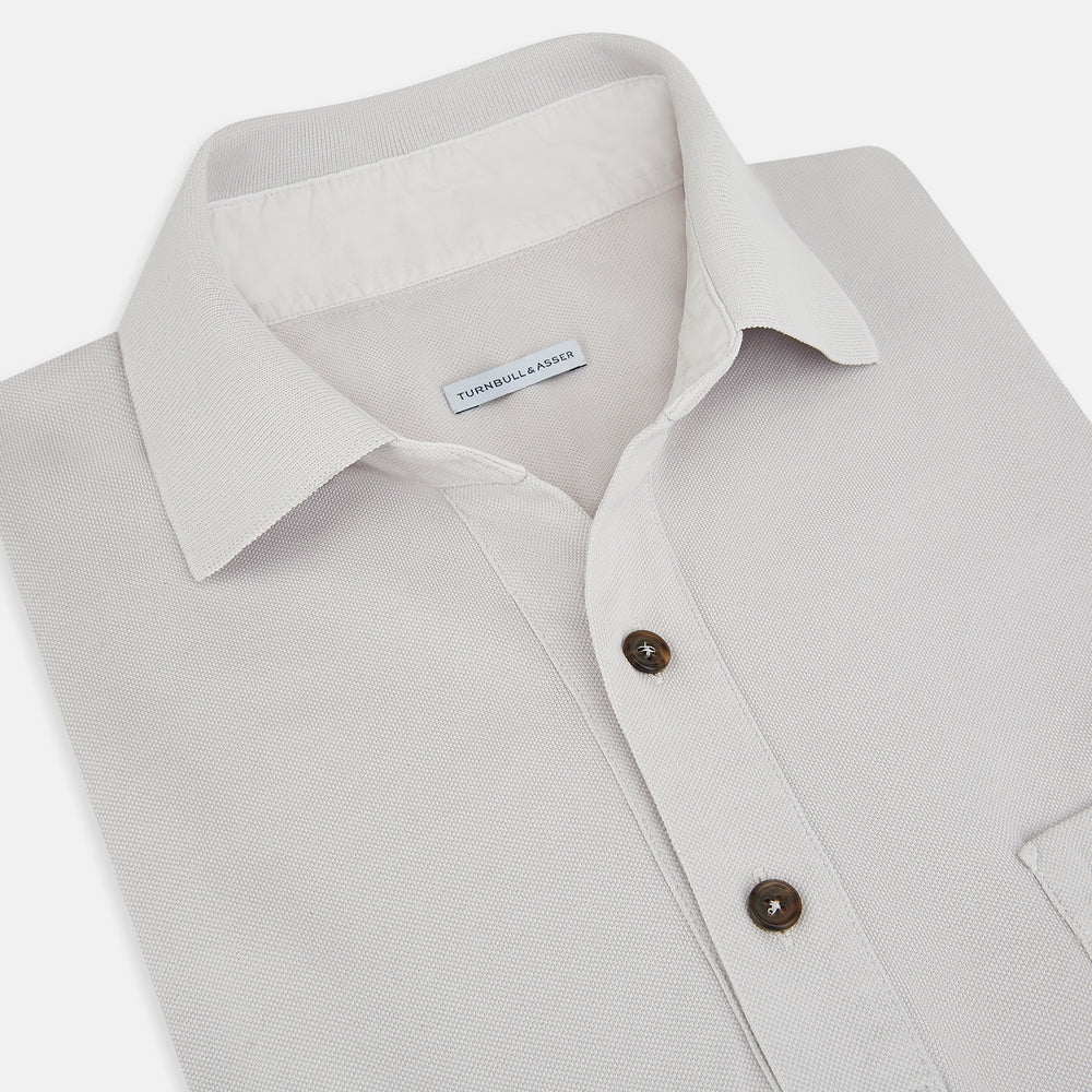 The Turnbull & Asser Pale Pink Polo Shirt is a cotton jersey short-sleeve polo with a collar, three brown buttons on the placket, and a button-flap chest pocket, shown against a white background.
