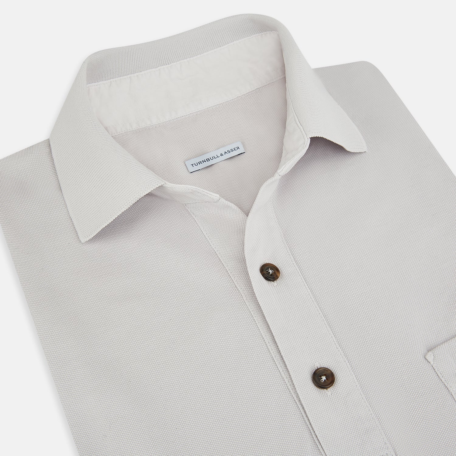 View 2 of product The Turnbull & Asser Pale Pink Polo Shirt is a cotton jersey short-sleeve polo with a collar, three brown buttons on the placket, and a button-flap chest pocket, shown against a white background.