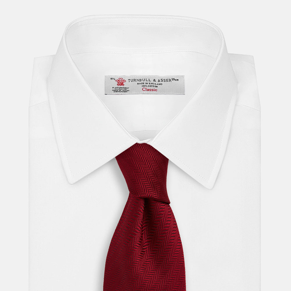 The Turnbull & Asser Plain Herringbone Burgundy Tie features a subtle pattern and rich color, making it an essential accessory for smart attire. Neatly rolled, it’s elegantly displayed on a plain white background.