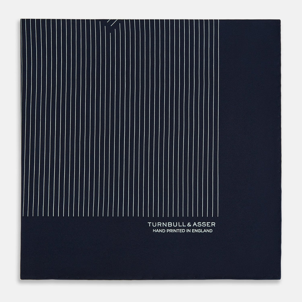 The Navy and White Stripe Silk Pocket Square by Turnbull & Asser features thin white vertical stripes and "TURNBULL & ASSER HAND PRINTED IN ENGLAND" in one corner, with a folded edge showing the reverse of this elegant silk accessory.