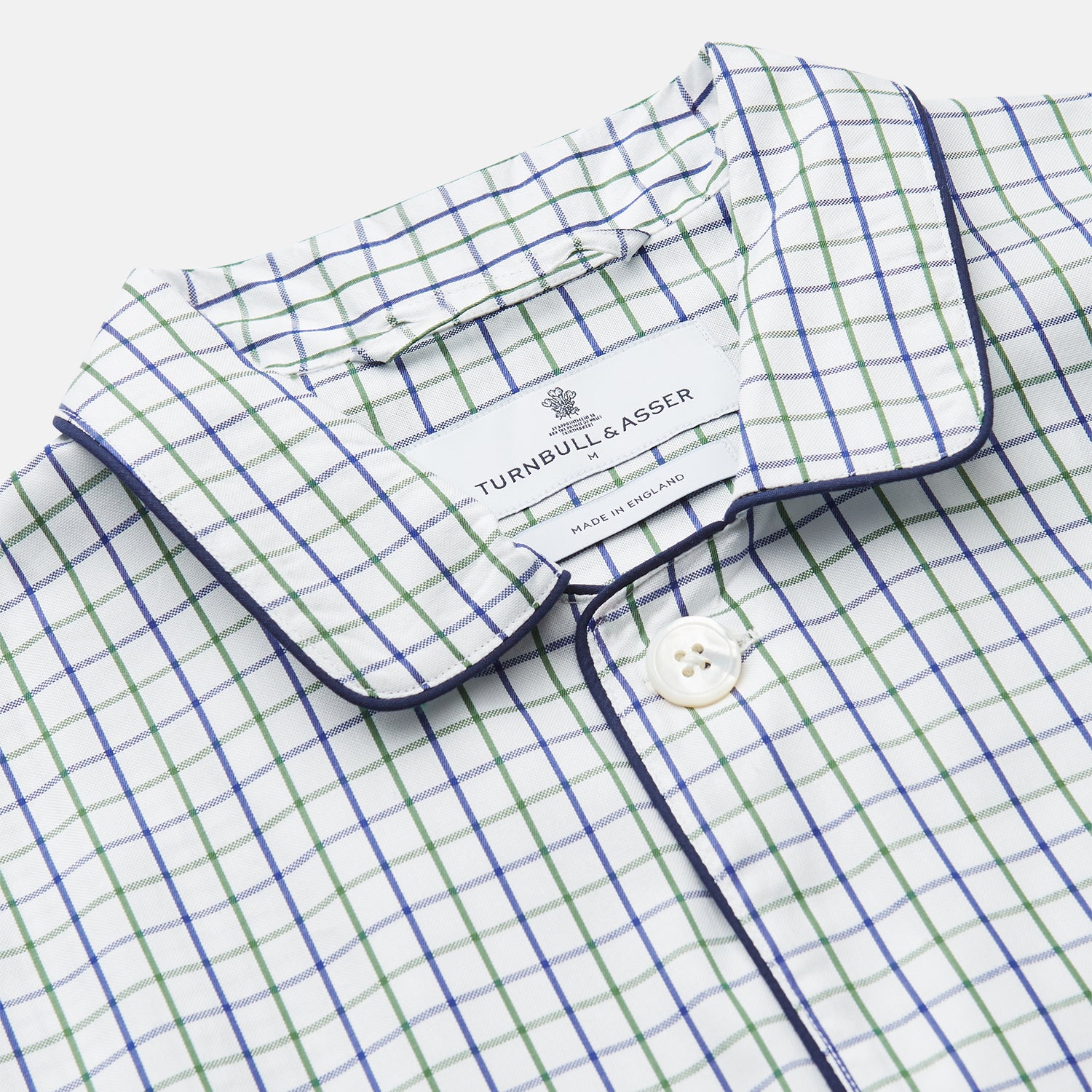 View 2 of product The Turnbull & Asser Green and Blue Check Cotton Hyde Pyjama Set for men features a long-sleeve, button-up top and pants with contrasting dark piping, shown laid flat on a white background.