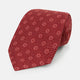 The Turnbull & Asser Red Medallion Silk Tie features a rolled-up red silk design with a repeating geometric pattern of small white circles and cross motifs on a plain white background.