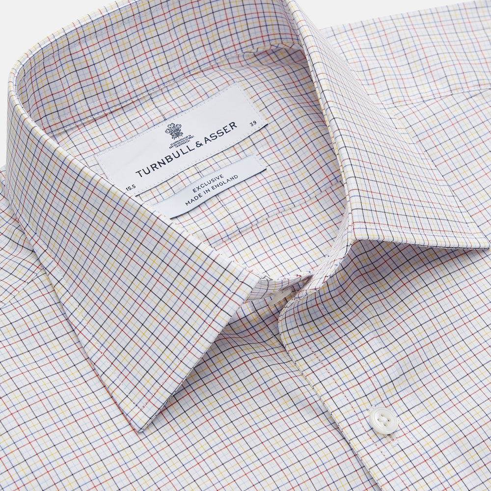 A man stands against a beige background, facing forward with a neutral expression and arms relaxed, wearing the Turnbull & Asser Red Multi Check Regular Fit Mayfair Shirt.