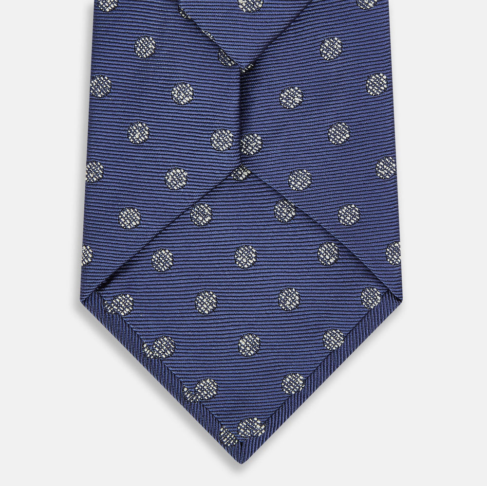 The Turnbull & Asser Navy Circle Silk Tie, made from pure silk with a navy base and small white dot pattern, is shown rolled up on a plain white background.
