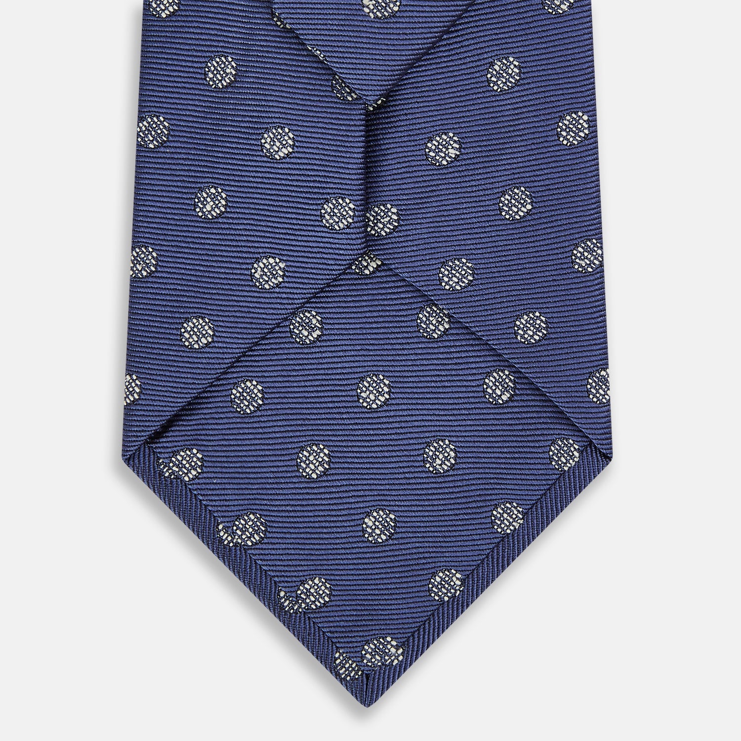 View 3 of product The Turnbull & Asser Navy Circle Silk Tie, made from pure silk with a navy base and small white dot pattern, is shown rolled up on a plain white background.