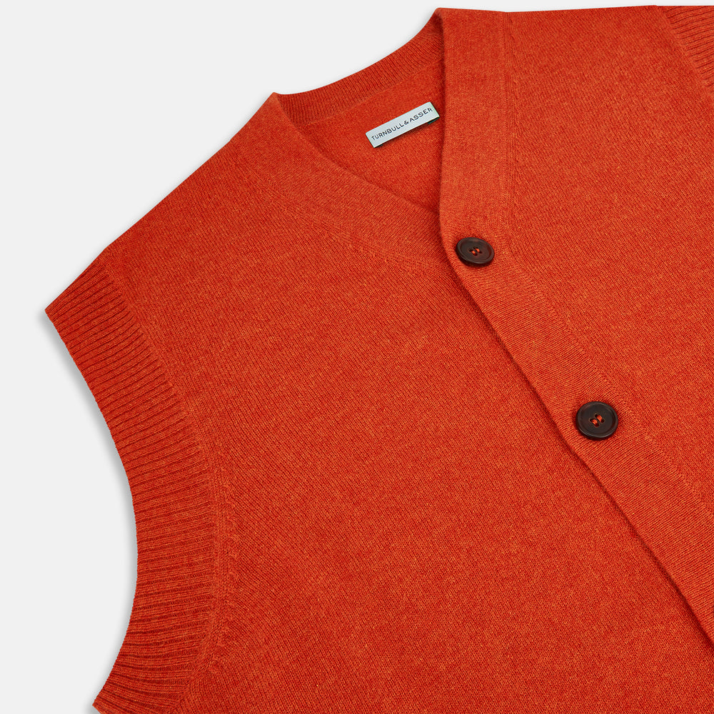 The Turnbull & Asser Red Orange Cashmere Sleeveless Cardigan features a ribbed collar, hem, and armholes, button-down front, and two front pockets—perfect as a refined light layer, shown against a white background.