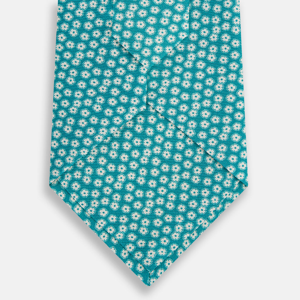 The Turnbull & Asser Turquoise Flower Patterned Silk Tie, featuring small white flowers, is shown rolled up on a white background.