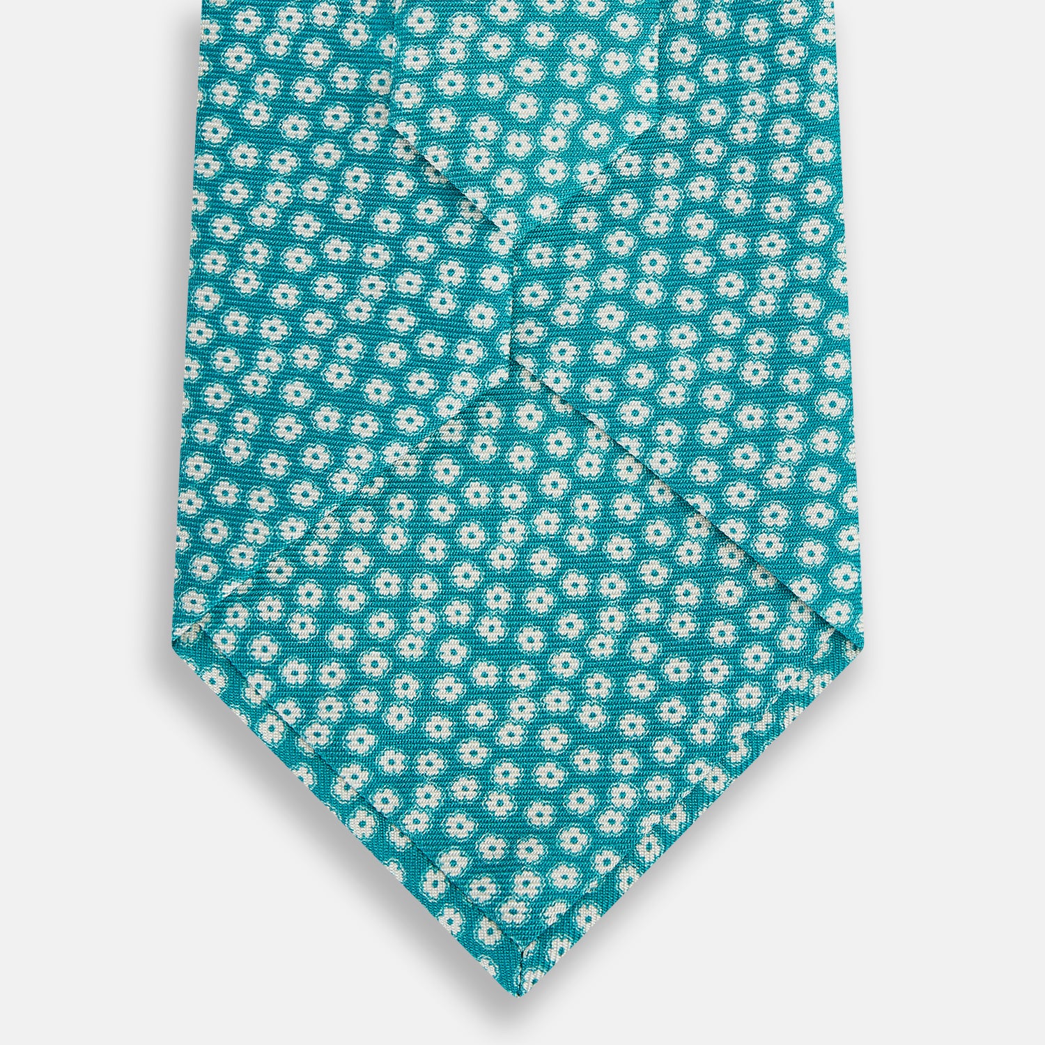 View 3 of product The Turnbull & Asser Turquoise Flower Patterned Silk Tie, featuring small white flowers, is shown rolled up on a white background.