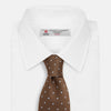 View 3 of product The LACE ON TONE SPOT EARTH RIVER TIE by Turnbull & Asser is a brown woven tie with small light blue dots, shown rolled up on a white background—a stylish accessory for formal outfits.