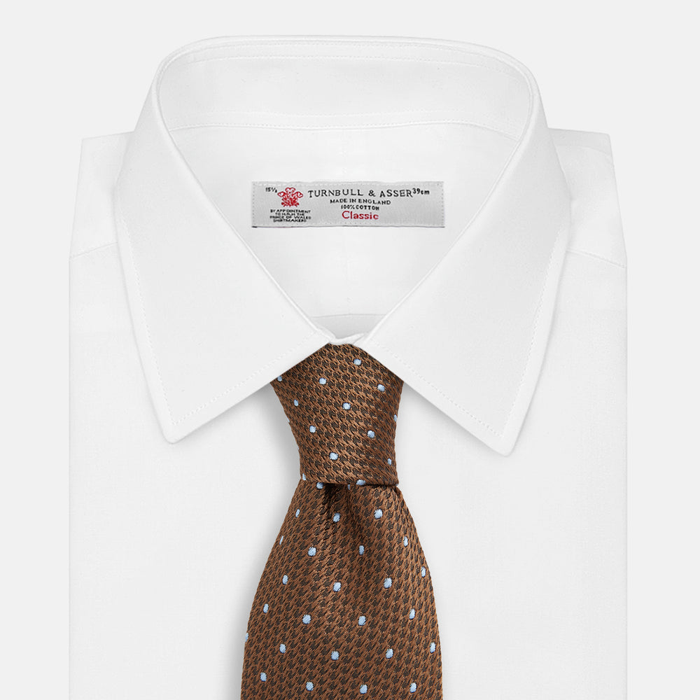 The LACE ON TONE SPOT EARTH RIVER TIE by Turnbull & Asser is a brown woven tie with small light blue dots, shown rolled up on a white background—a stylish accessory for formal outfits.