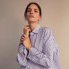 View 6 of product The Turnbull & Asser Pale Blue Candy Stripe Cotton Marlene Shirt is an oversized women's collared shirt with long sleeves, buttoned cuffs, and vertical blue and white stripes, shown laid flat on a white background.