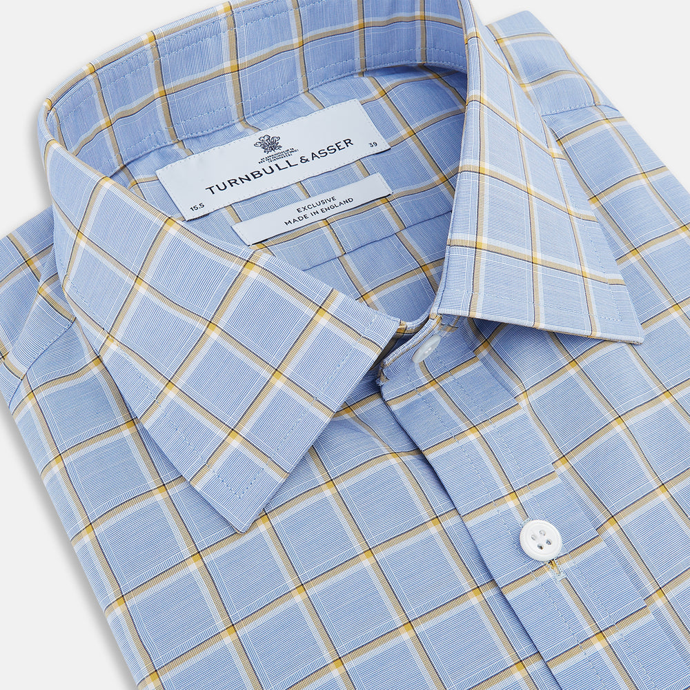 The Turnbull & Asser Blue and Yellow Windowpane Mayfair Shirt is crafted from fine Italian cotton, featuring a light blue base with yellow and white checks, shown on a plain white background.