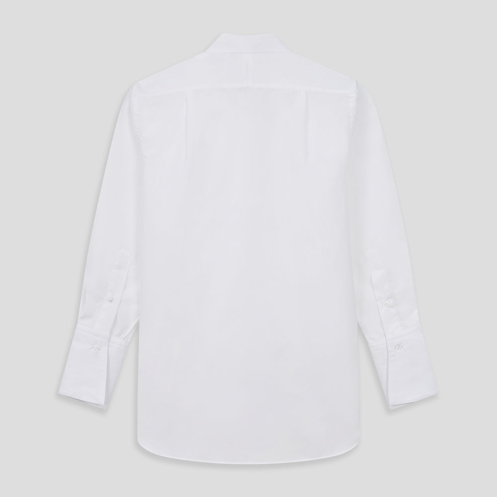 A person with curly hair wears the Turnbull and The Deck White Cotton Minimalist Shirt by Turnbull & Asser, paired with pants. Posed against a plain background, their minimalist silhouette is highlighted in this black and white image.