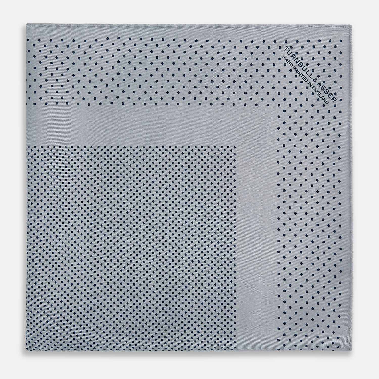 View 8 of product The Turnbull & Asser Grey Dot Silk Pocket Square features a light gray silk design with navy polka dots and a solid border. Elegantly handmade, it is shown with one corner folded to display both sides.