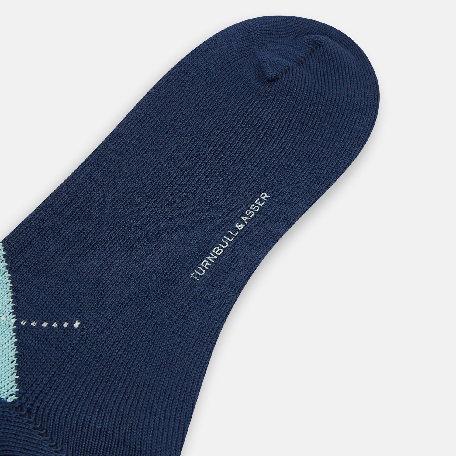View 3 of product The Azzurro Wool Check Mid-Length Socks by Turnbull & Asser are navy blue with a ribbed cuff, featuring an argyle pattern in light blue, teal, and navy with white accents. Displayed upright against a plain white background.