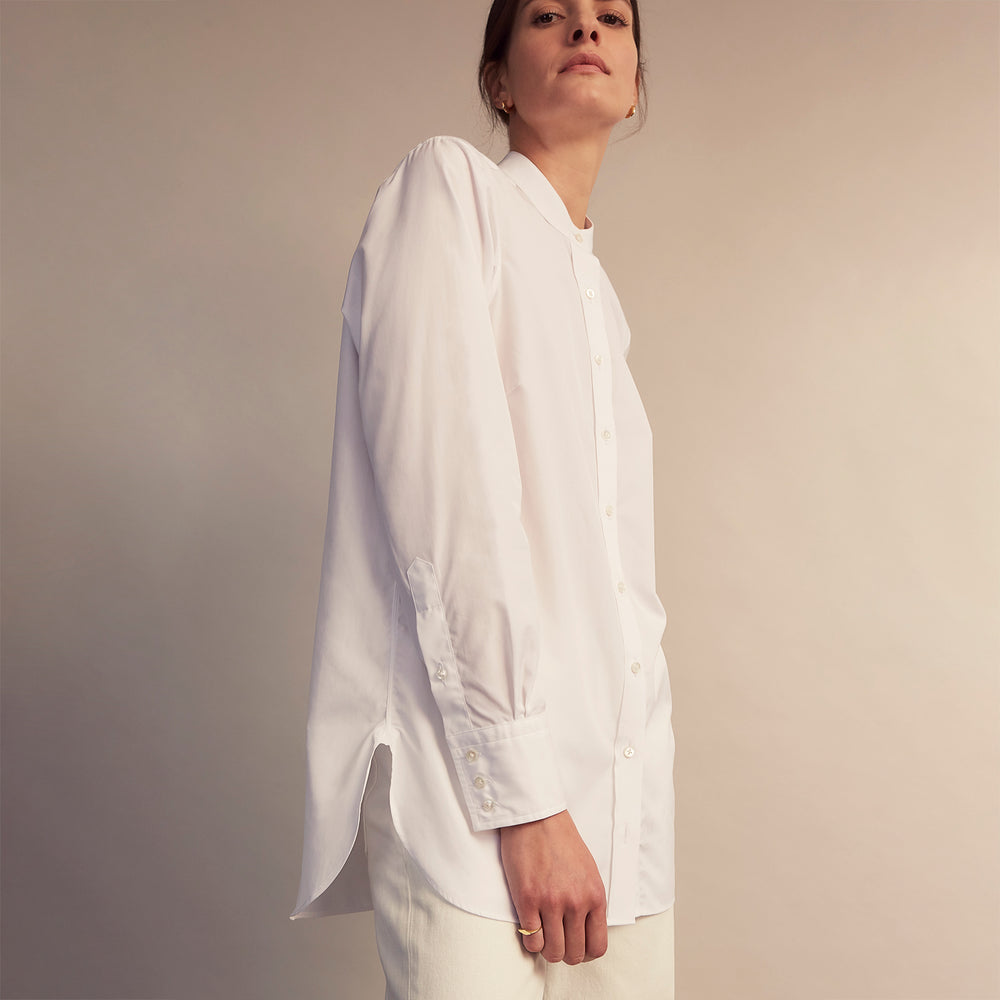The White Cotton Lauren Shirt by Turnbull & Asser, featuring a stand collar, button-down front, and elongated body, is laid flat on a plain white background.