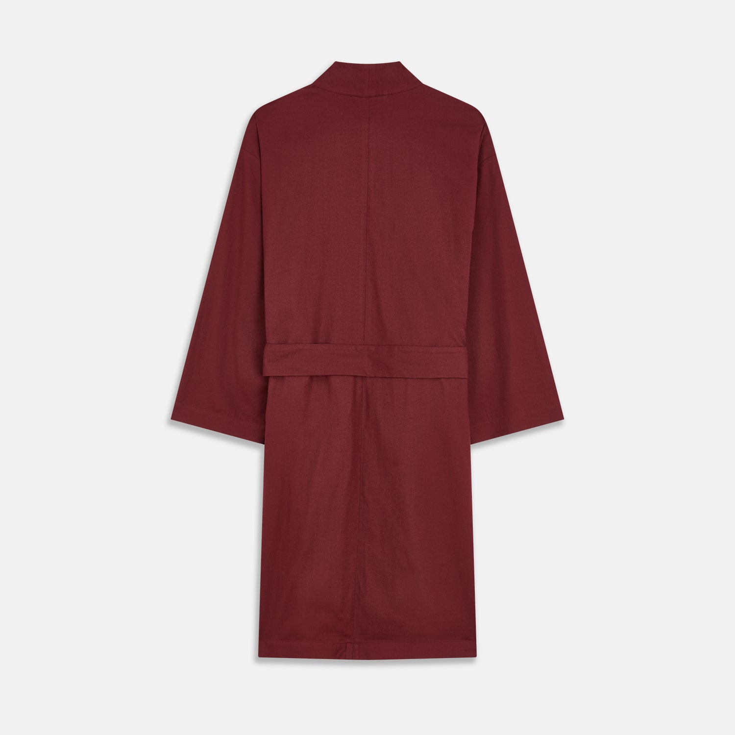 View 5 of product A person stands indoors by a window, wearing the Turnbull & Asser Burgundy Cotton-Cashmere Kimono Gown over striped pajamas, with matching slippers, next to cream curtains and a wooden chair against a pale wall.