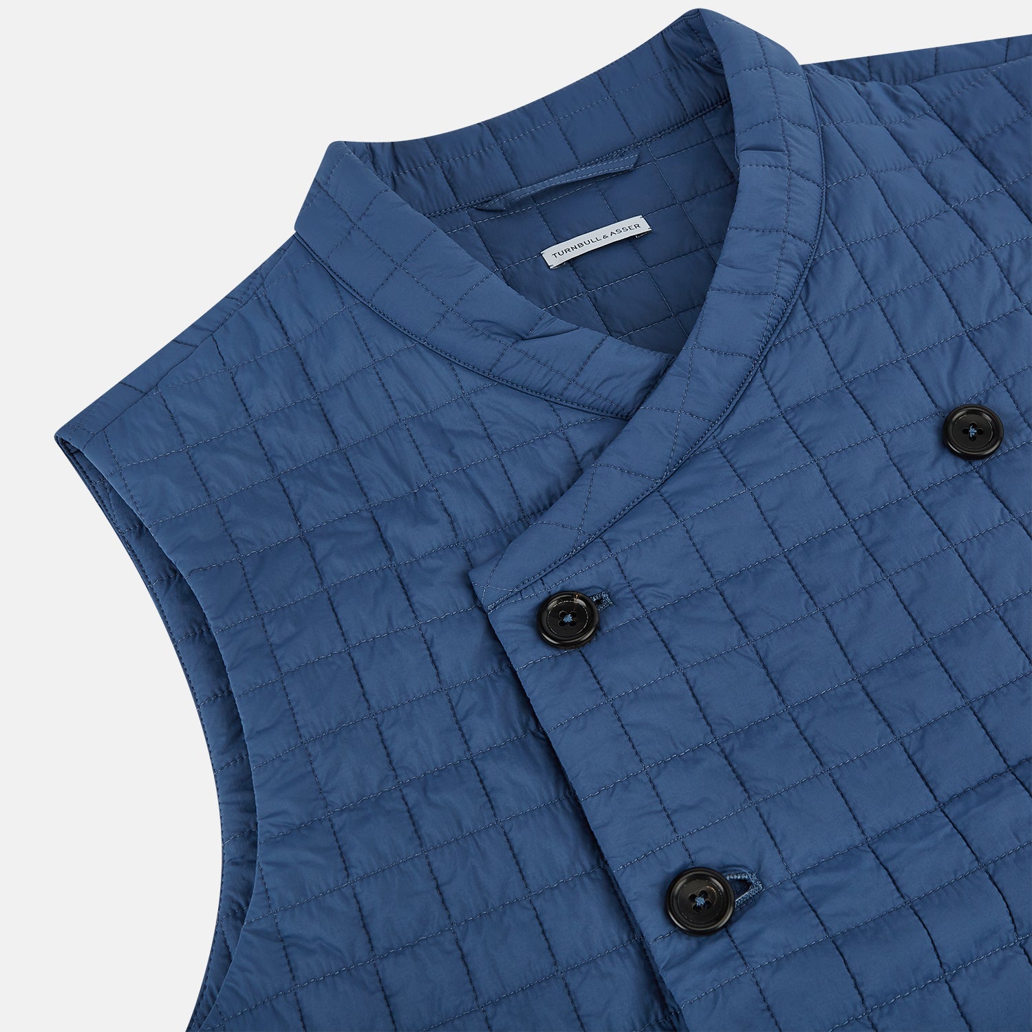 View 2 of product The Azzurro Double-Breasted Quilted Gilet by Turnbull & Asser is a sleeveless blue piece with black buttons, two zippered pockets, and a chest pocket—ideal for layered looks against a plain white background.