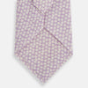 View 3 of product The Turnbull & Asser Lilac Flower Patterned Silk Tie features a light pink hue with a repeating white floral motif, shown rolled up on a plain white background.