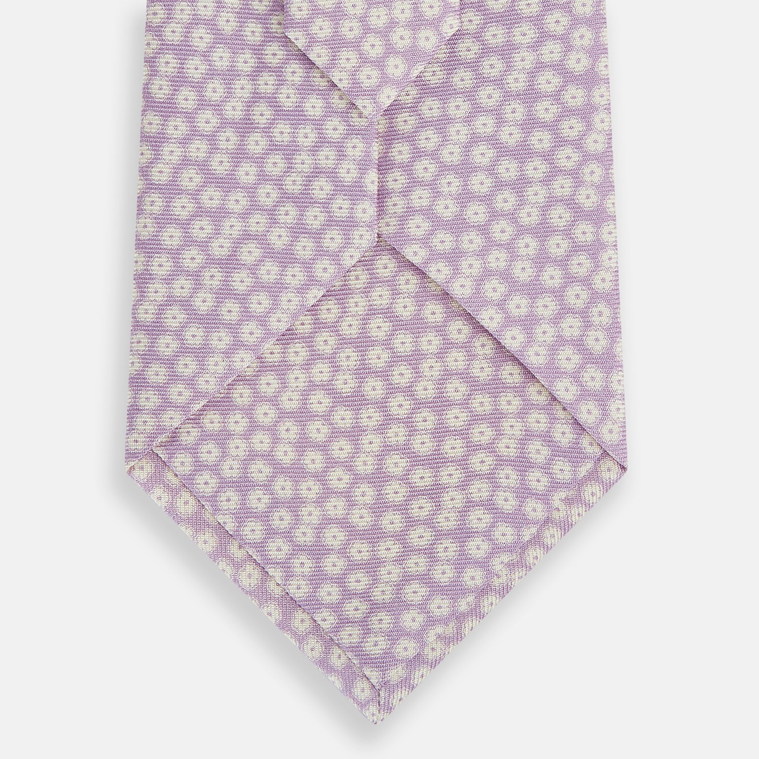 View 3 of product The Turnbull & Asser Lilac Flower Patterned Silk Tie features a light pink hue with a repeating white floral motif, shown rolled up on a plain white background.