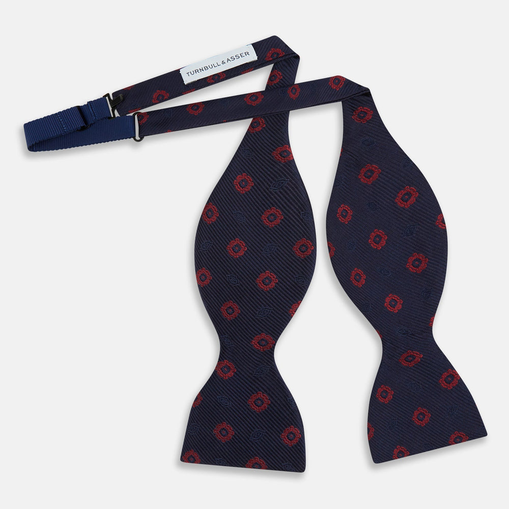 Elevate your formalwear with the Turnbull & Asser Navy and Burgundy Motif Silk Bow Tie, featuring a subtle ribbed texture and repeating red geometric motifs.
