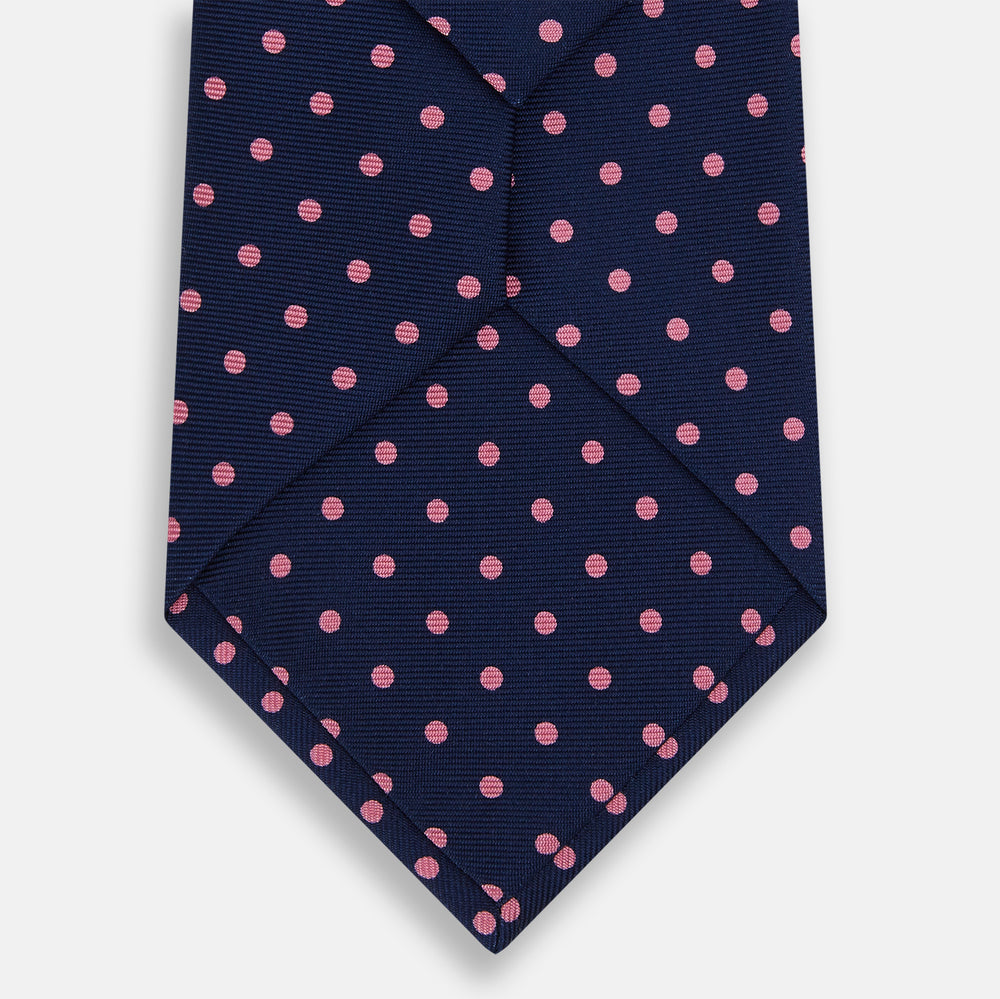 The Pink Dot and Navy Silk Tie by Turnbull & Asser features evenly spaced pink polka dots on navy silk, rolled neatly on a white background—a classic British style ideal for refined occasions.
