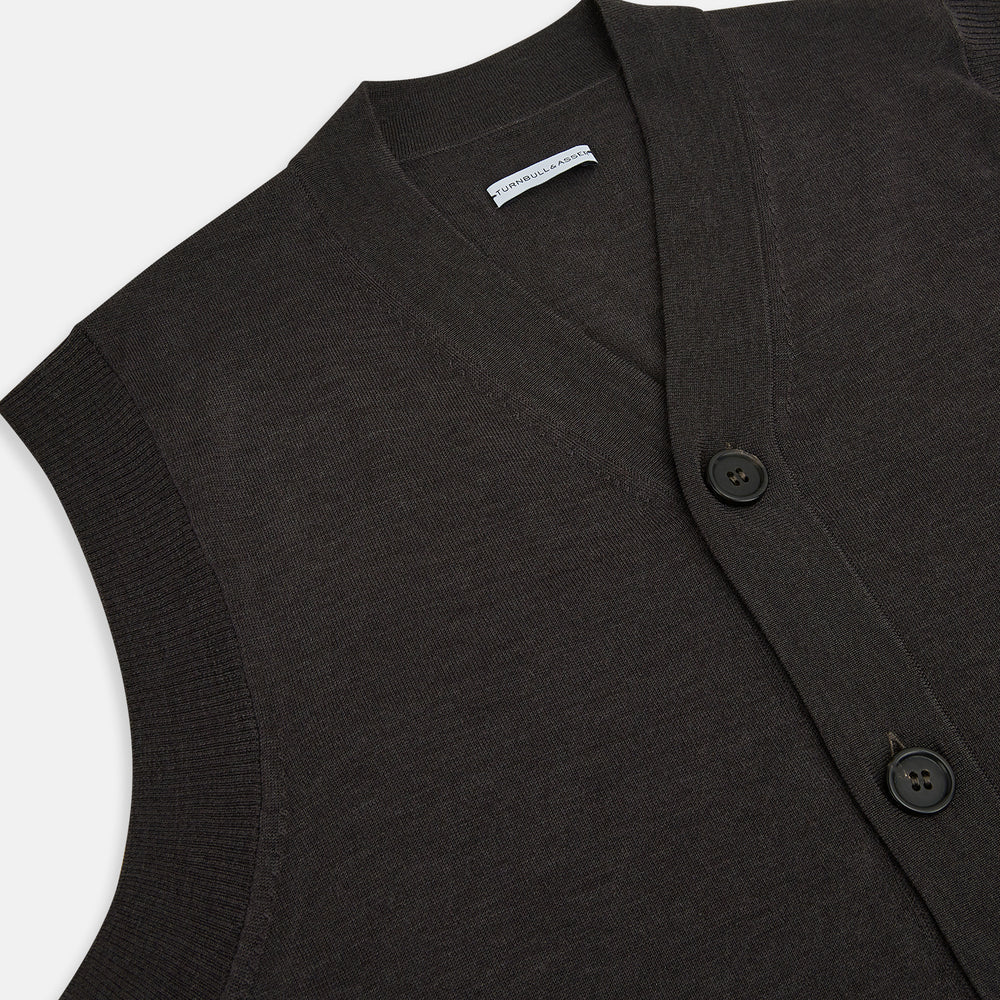 The Turnbull & Asser Dark Brown Merino V-Neck Sleeveless Cardigan features a button-up front and two pockets, styled as a men's sleeveless vest and shown on a plain white background.