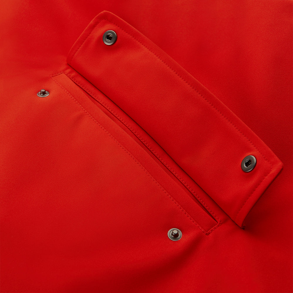 Wearing the Turnbull & Asser Red Walter Sealup Parka with Detachable Liner, black pants, and white sneakers, a person stands in profile against a plain light background—perfect for travel.
