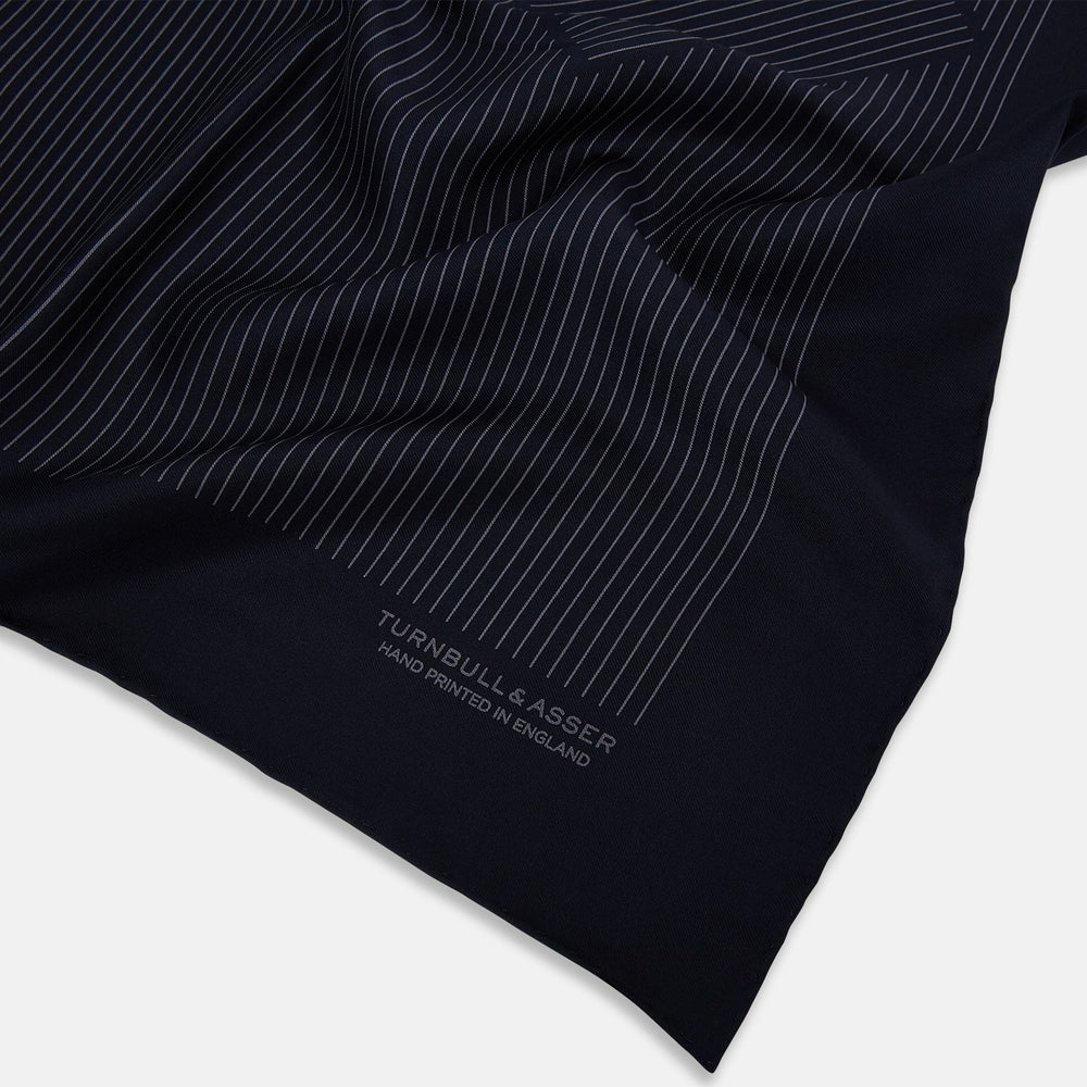 The Navy and Charcoal Stripe Silk Pocket Square by Turnbull & Asser features fine hand-rolled edges, thin white stripes on navy, and TURNBULL & ASSER HAND PRINTED IN ENGLAND in white on the corner.