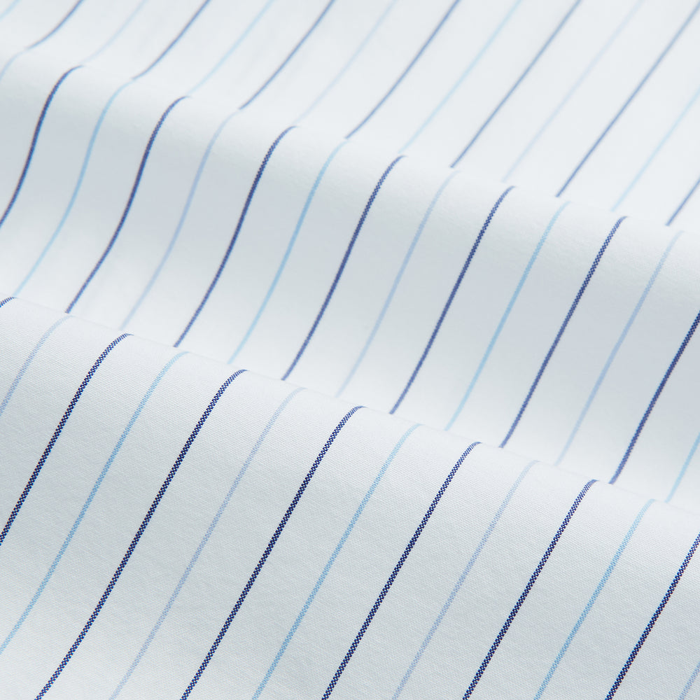The Turnbull & Asser Blue Wide Pinstripe Mayfair Shirt is a long-sleeved, collared, button-down style crafted from organic cotton, featuring wide blue pinstripes on a white background.