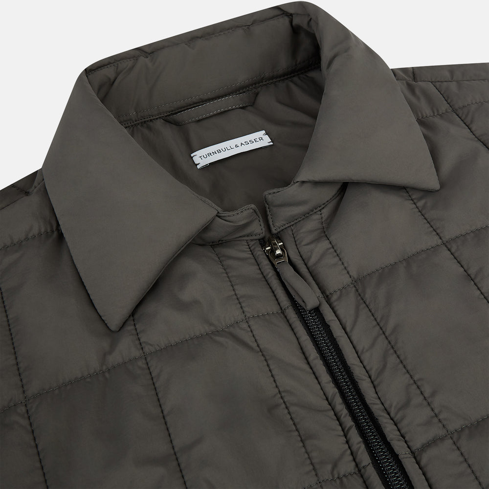 The Battersea Shadow Grey Quilted Jacket by Turnbull & Asser features a front zipper, buttoned cuffs, pointed collar, and multiple pockets—an ideal choice for the modern gentleman. Shown on a plain white background.