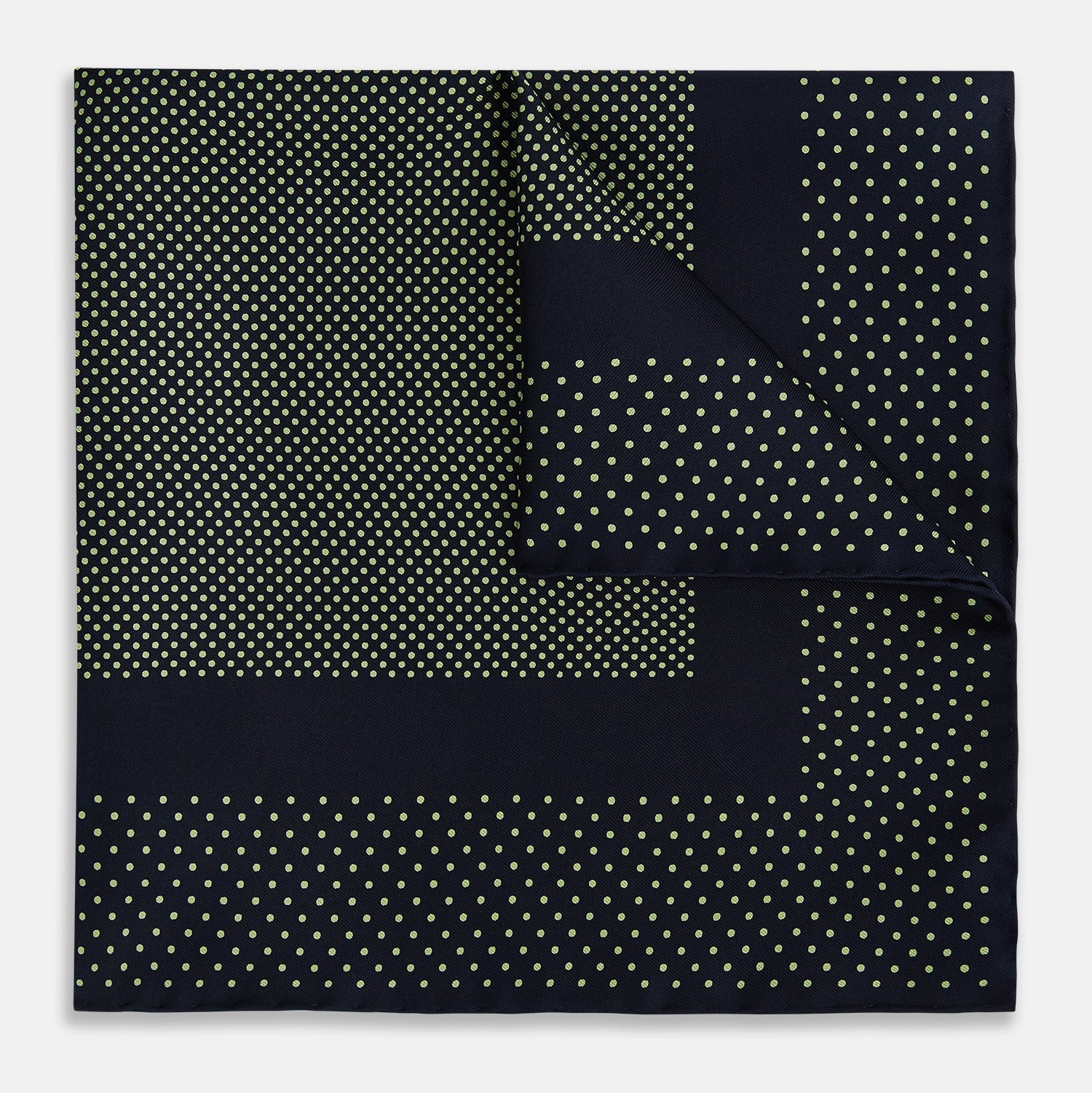 View 1 of product The Turnbull & Asser Navy and Melon Green Dot Silk Pocket Square features small melon green dots on navy silk with a solid border. One corner is folded over to highlight its exquisite handmade craftsmanship.