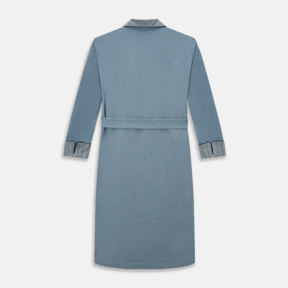 The Turnbull & Asser Blue Stripe Collar Cotton Twill Gown features a light blue hue, striped collar and cuffs, long sleeves, patch pockets, and a matching belt for elevated home comfort. Shown on a white background.