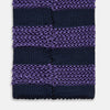 View 4 of product The KNITTED STRIPE PURPLE TIE by Turnbull & Asser features bold dark blue and purple stripes, making it an essential smart accessory. Shown rolled up on a white background.