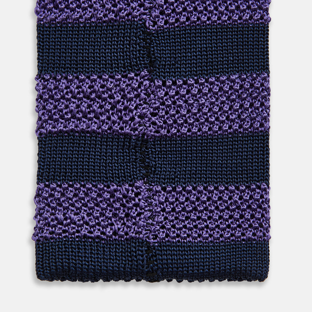 The KNITTED STRIPE PURPLE TIE by Turnbull & Asser features bold dark blue and purple stripes, making it an essential smart accessory. Shown rolled up on a white background.