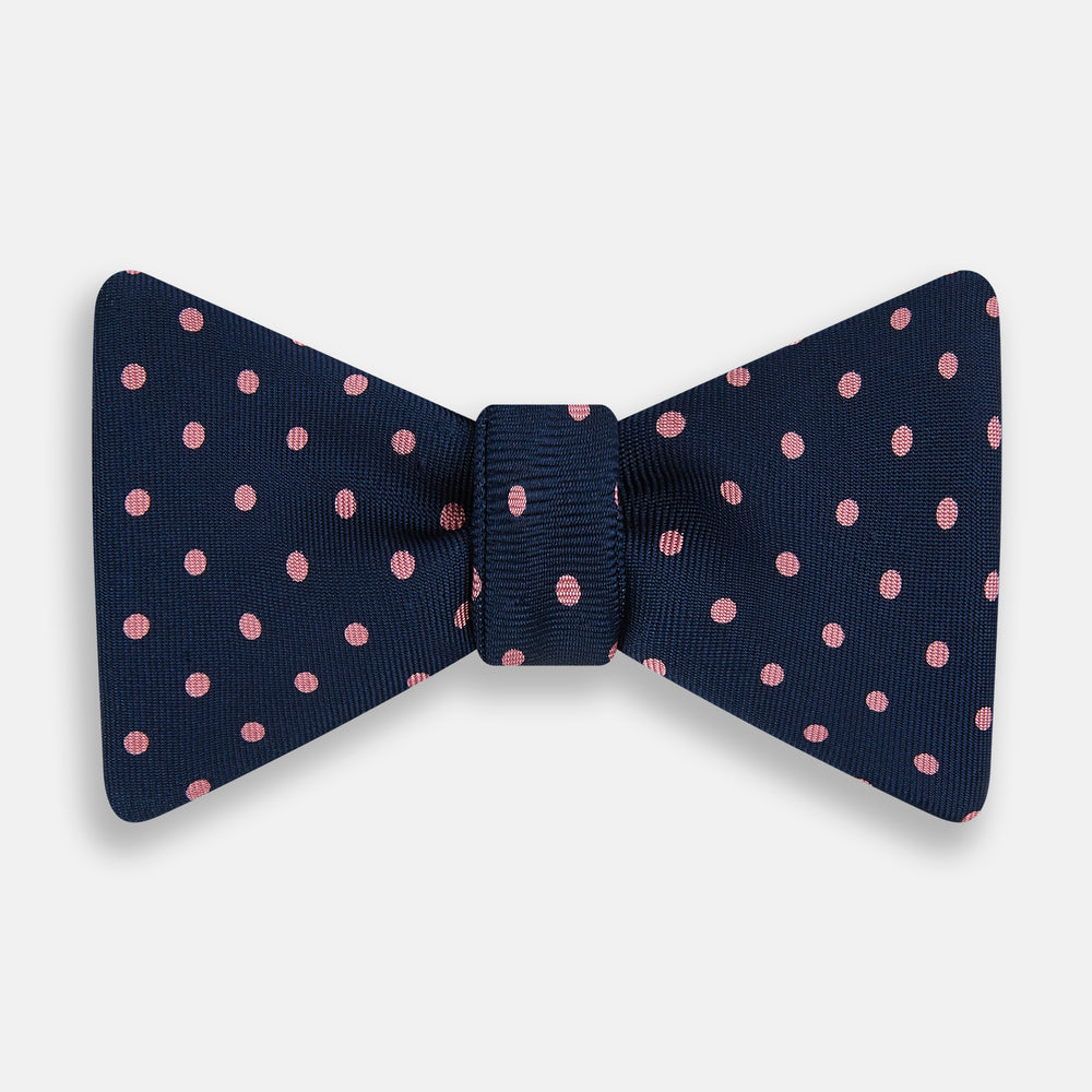 The Navy and Pink Spot Silk Bow Tie by Turnbull & Asser features evenly spaced pink polka dots on navy silk, shown against a plain white background.