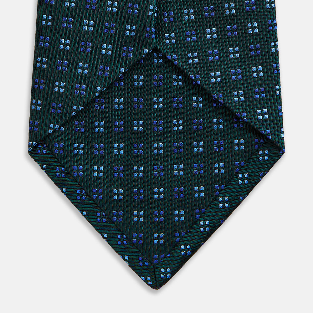 The MINI SQUARE SPOT FOREST GREEN BLUE TIE by Turnbull & Asser is a classic men's accessory, featuring a rolled-up green silk design with small blue geometric patterns—perfect for the modern gentleman.