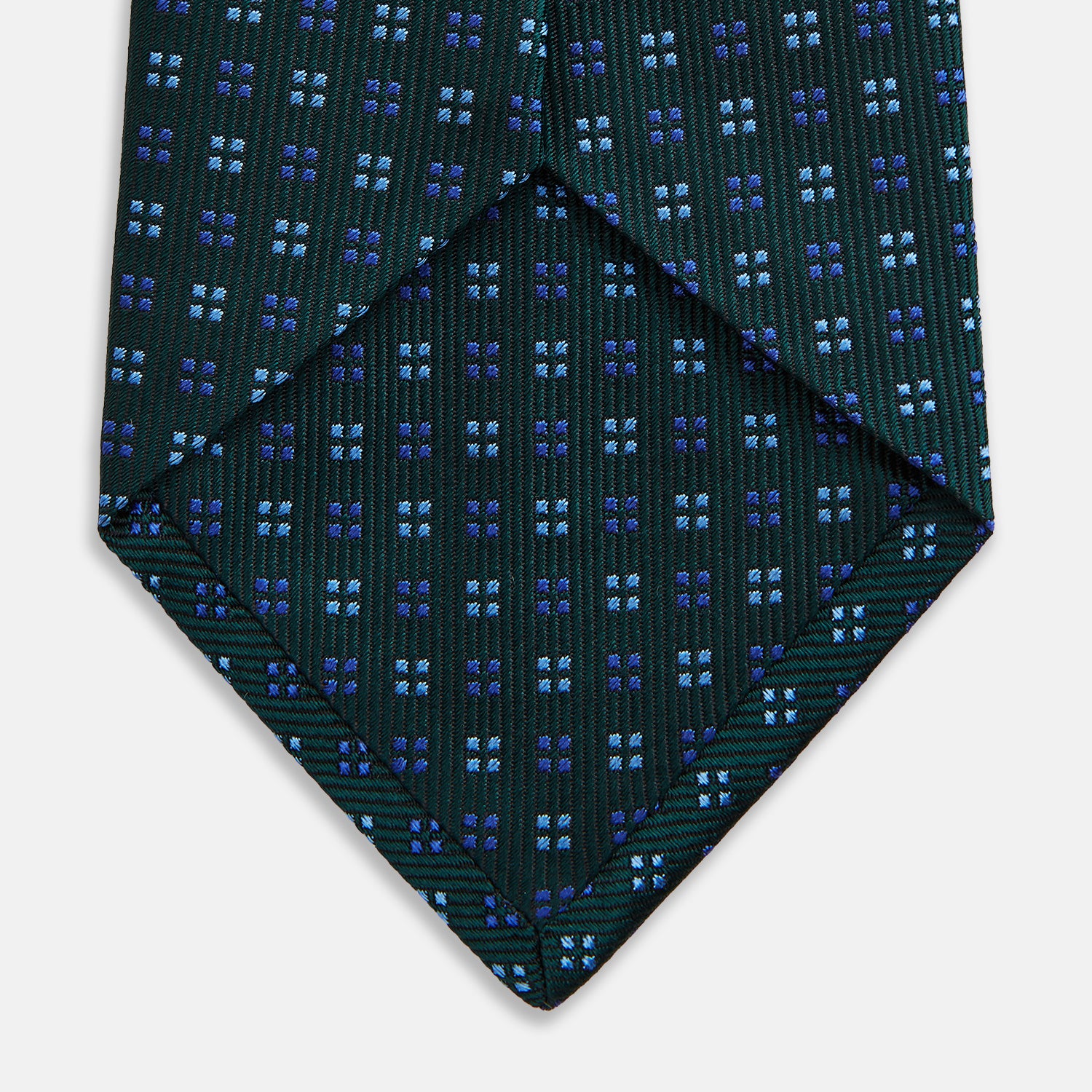 View 4 of product The MINI SQUARE SPOT FOREST GREEN BLUE TIE by Turnbull & Asser is a classic men's accessory, featuring a rolled-up green silk design with small blue geometric patterns—perfect for the modern gentleman.