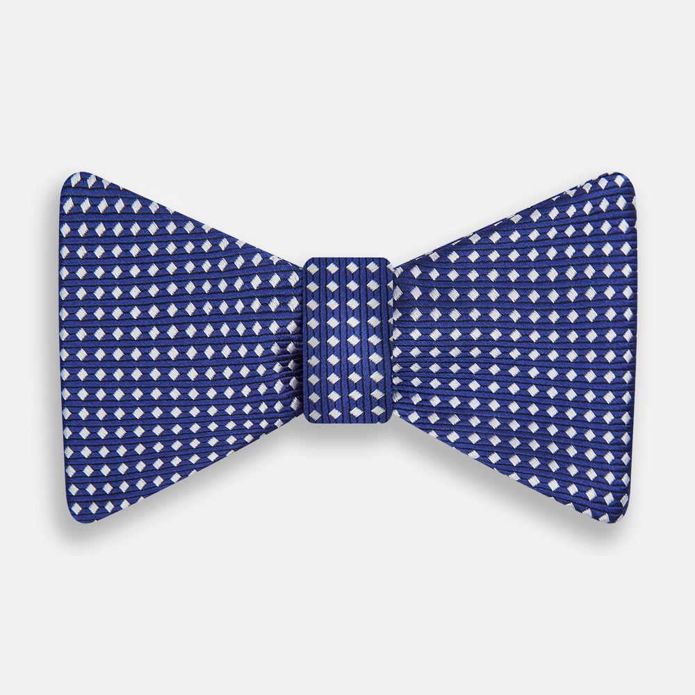 The Turnbull & Asser Blue and White Diamond Silk Bow Tie features a repeating pattern of small white diamonds and vertical ribbing, making it perfect for formalwear. Displayed on a white background.