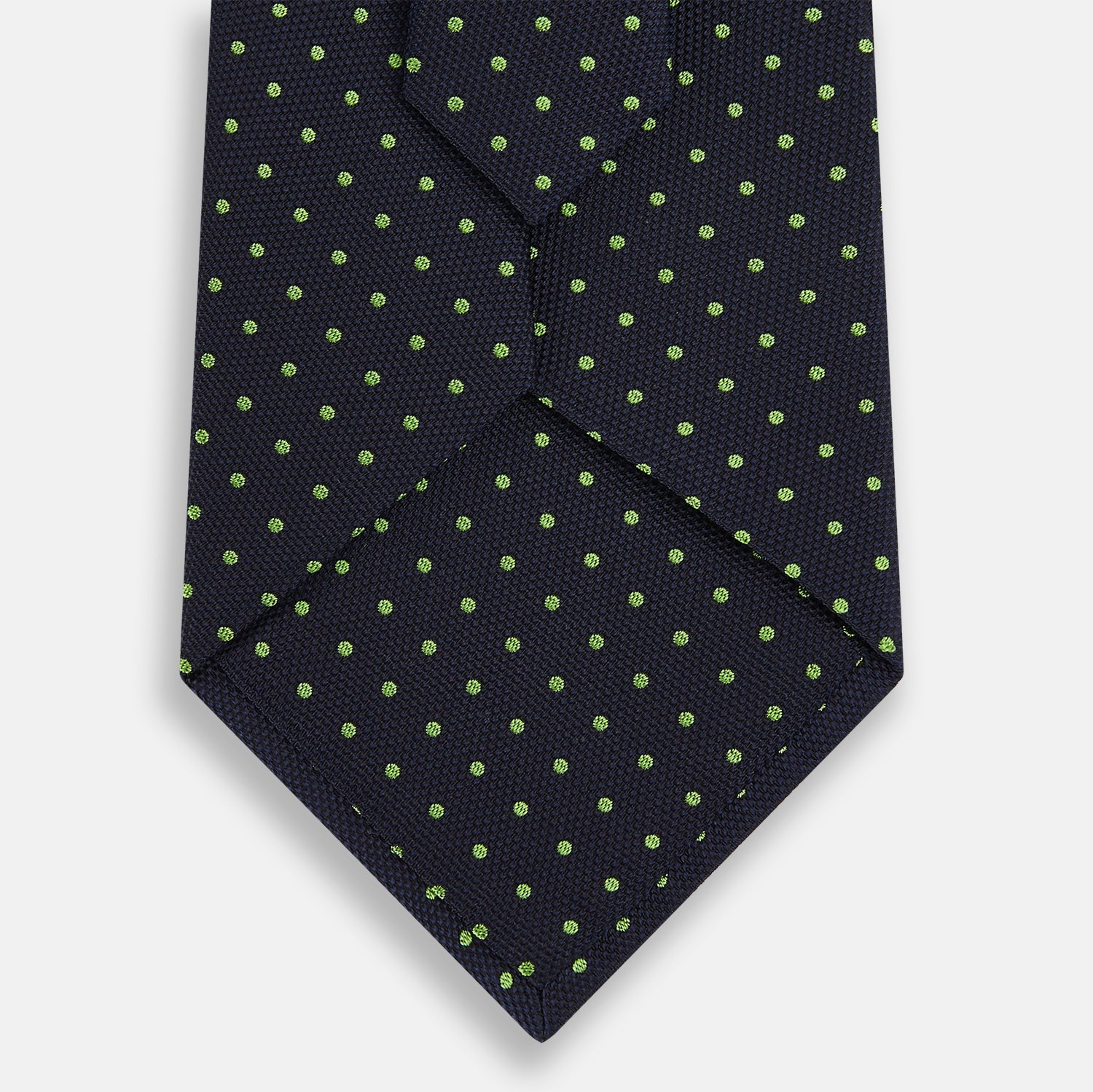 View 3 of product The Turnbull & Asser Green and Navy Micro Dot Silk Tie features small green dots on a navy silk background, displayed rolled up on white.