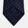 View 4 of product The LACE ON TONE SPOT NAVY FORD TIE by Turnbull & Asser is a rolled-up navy tie with textured fabric and an evenly spaced pattern of small light blue polka dots.
