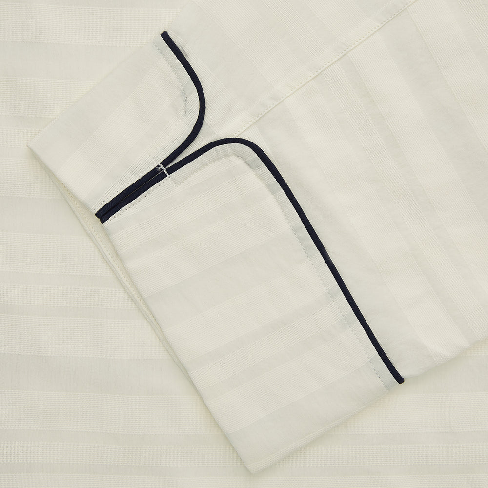 The Cream Pattern Cotton Blend Quin Pyjama Set by Turnbull & Asser features cream stripes, a long-sleeve button-up camp collar shirt with a chest pocket and black piping, and matching drawstring pants.