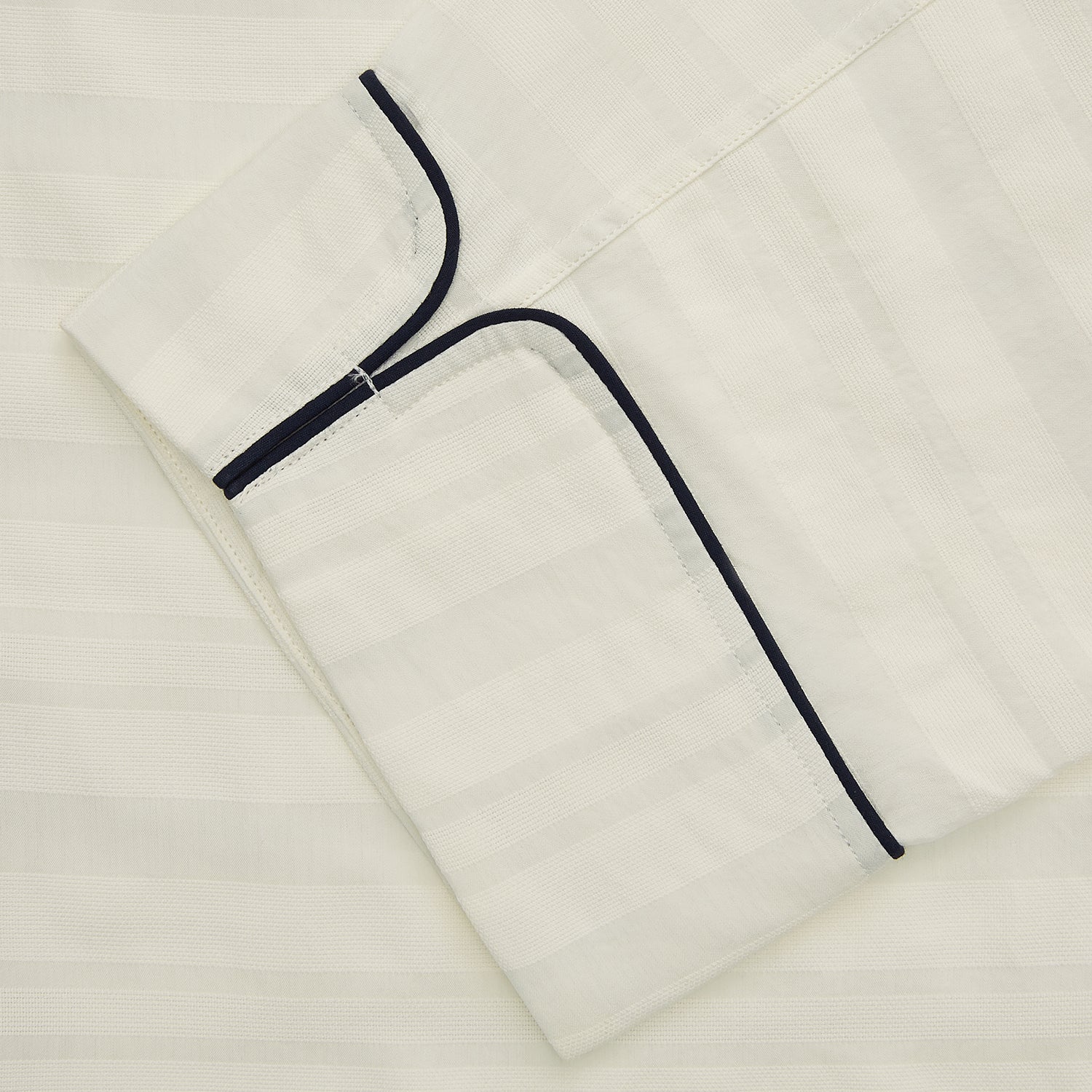 View 3 of product The Cream Pattern Cotton Blend Quin Pyjama Set by Turnbull & Asser features cream stripes, a long-sleeve button-up camp collar shirt with a chest pocket and black piping, and matching drawstring pants.
