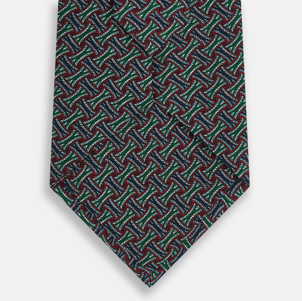 The Forest Green and Red Weave Patterned Silk Tie by Turnbull & Asser features a geometric interlocking design in red, blue, and green, elegantly rolled on a white background.