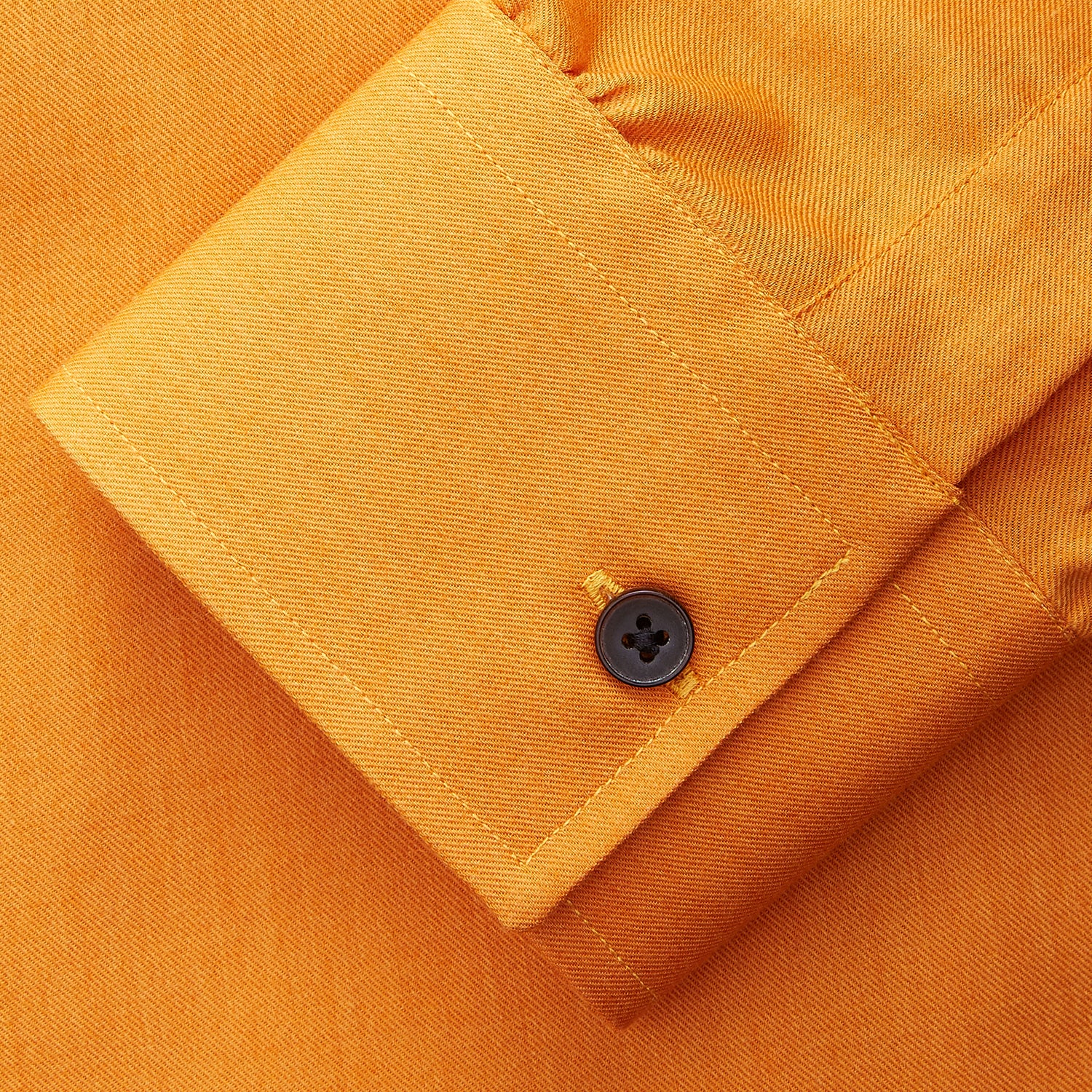 View 5 of product A man stands against a tan background, wearing a Turnbull & Asser Orange Weekend Fit Cotton & Wool Shirt with Derby Collar and 1 Button Cuffs, tucked into dark blue dress pants with a black belt and shoes. He has one hand in his pocket.