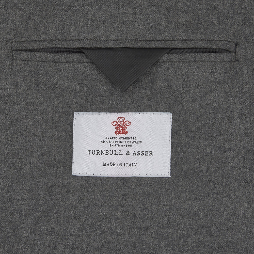 The Turnbull & Asser Grey Merino Wool Jacket is single-breasted with a notched lapel, two front patch pockets, and a single button closure, fashioned from fine Super Merino Wool. Shown here against a plain white background.