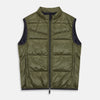 View 2 of product A man stands against a plain background wearing the Turnbull & Asser Green Peyton Sealup Quilted Gilet over a striped shirt, dark trousers, and white sneakers, with his hands in his pockets and looking slightly to the side.